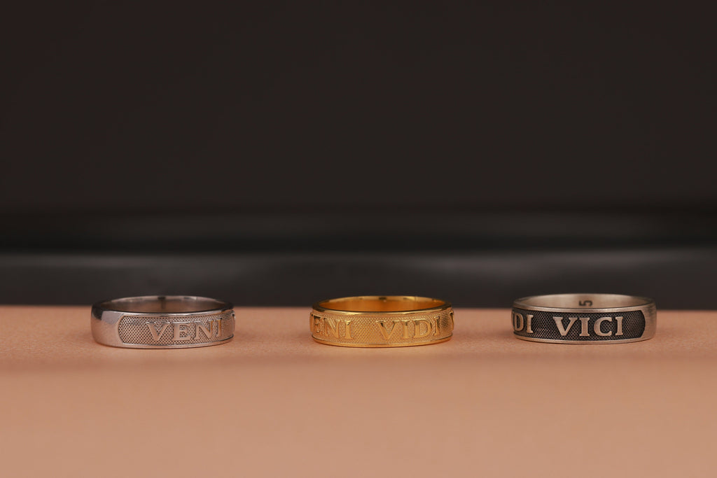 Three rings, two silver and one gold, on a brown surface with a dark background.