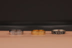 Three rings, two silver and one gold, on a brown surface with a dark background.