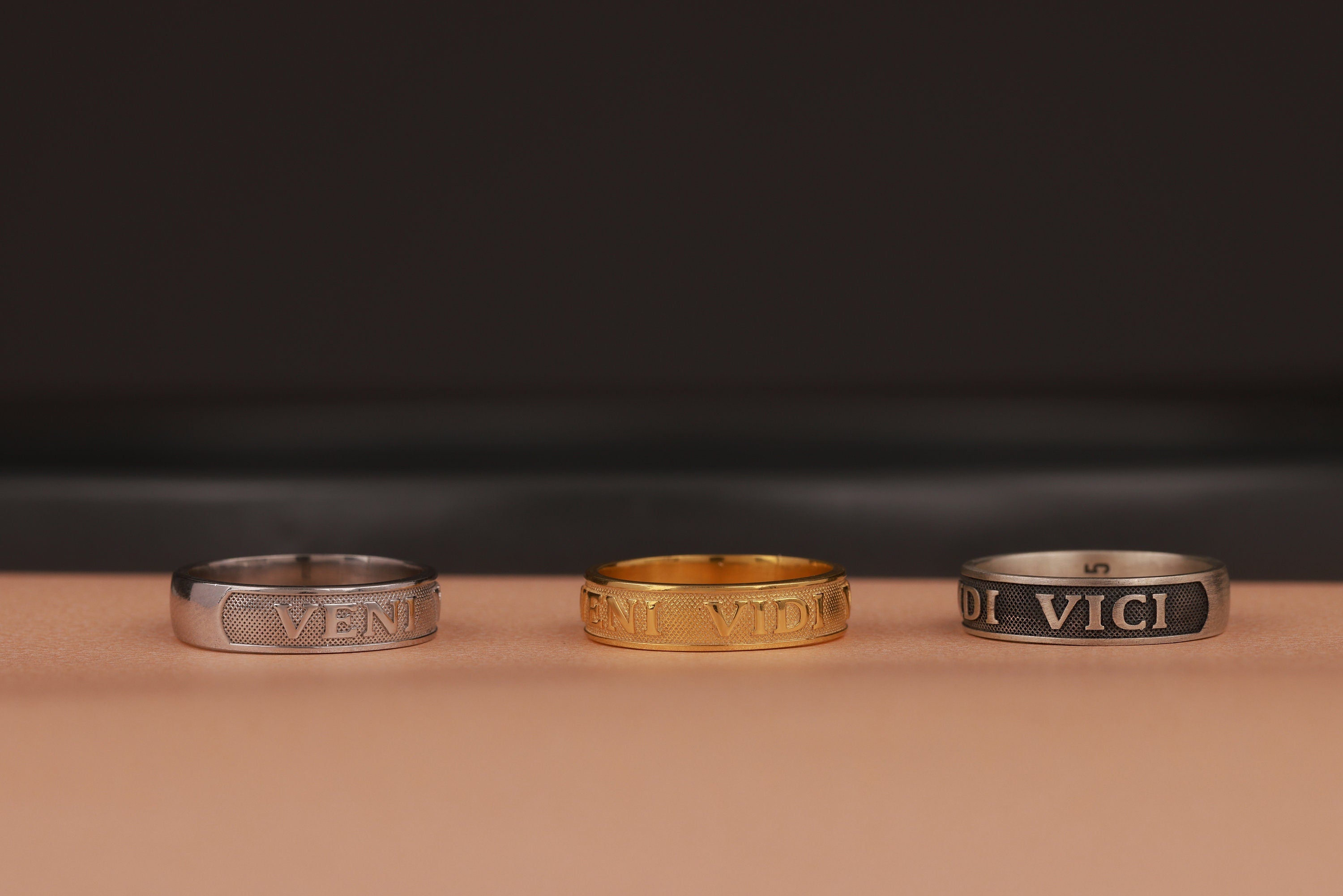 Three rings, two silver and one gold, on a brown surface with a dark background.