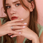 Close-up of a woman with a ring on her finger against a pink background