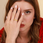Woman wearing a gold ring on her finger, with a neutral background