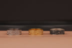 Three rings, one gold and two silver, on a brown surface with a dark background