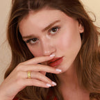 Woman with a gold ring on her finger against a beige background
