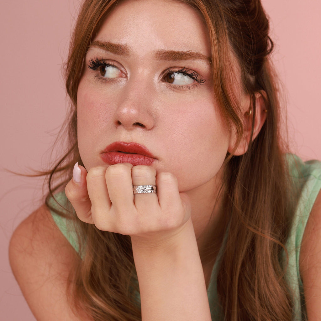Woman with a polished silver ring on her chin against a pink background