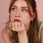 Woman with a polished silver ring on her chin against a pink background