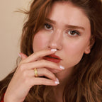 Close-up of a woman with a gold ring on her finger against a beige background