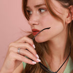 Close-up of a woman holding sunglasses with a pink background