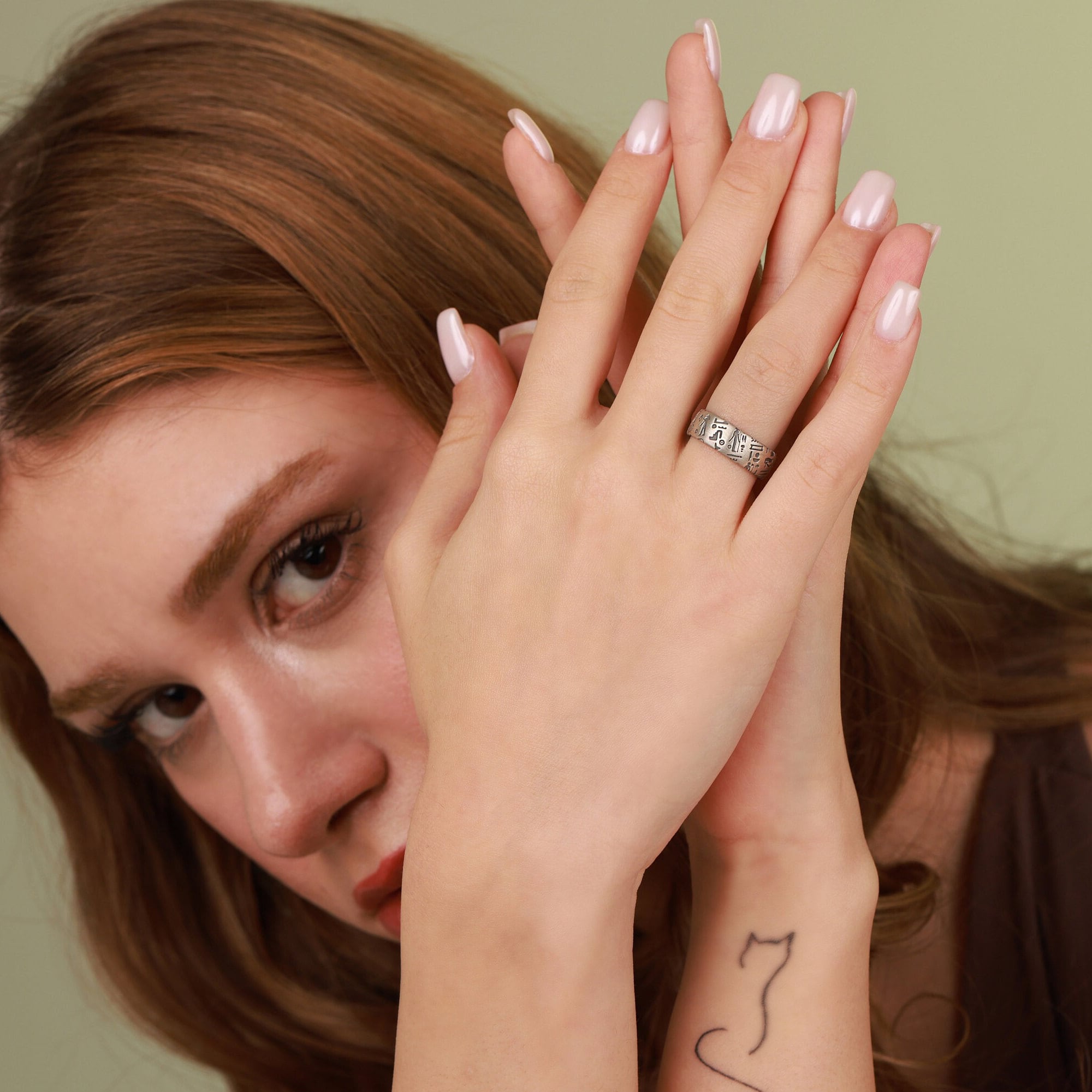 A woman wearing a ring with Egyptian symbols, holding her hands together.