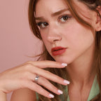 Close-up of a woman with a ring on her finger against a pink background