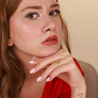 Woman with a gold ring on her finger against a beige background