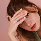 Woman with a polished silver ring on her finger against a pink background