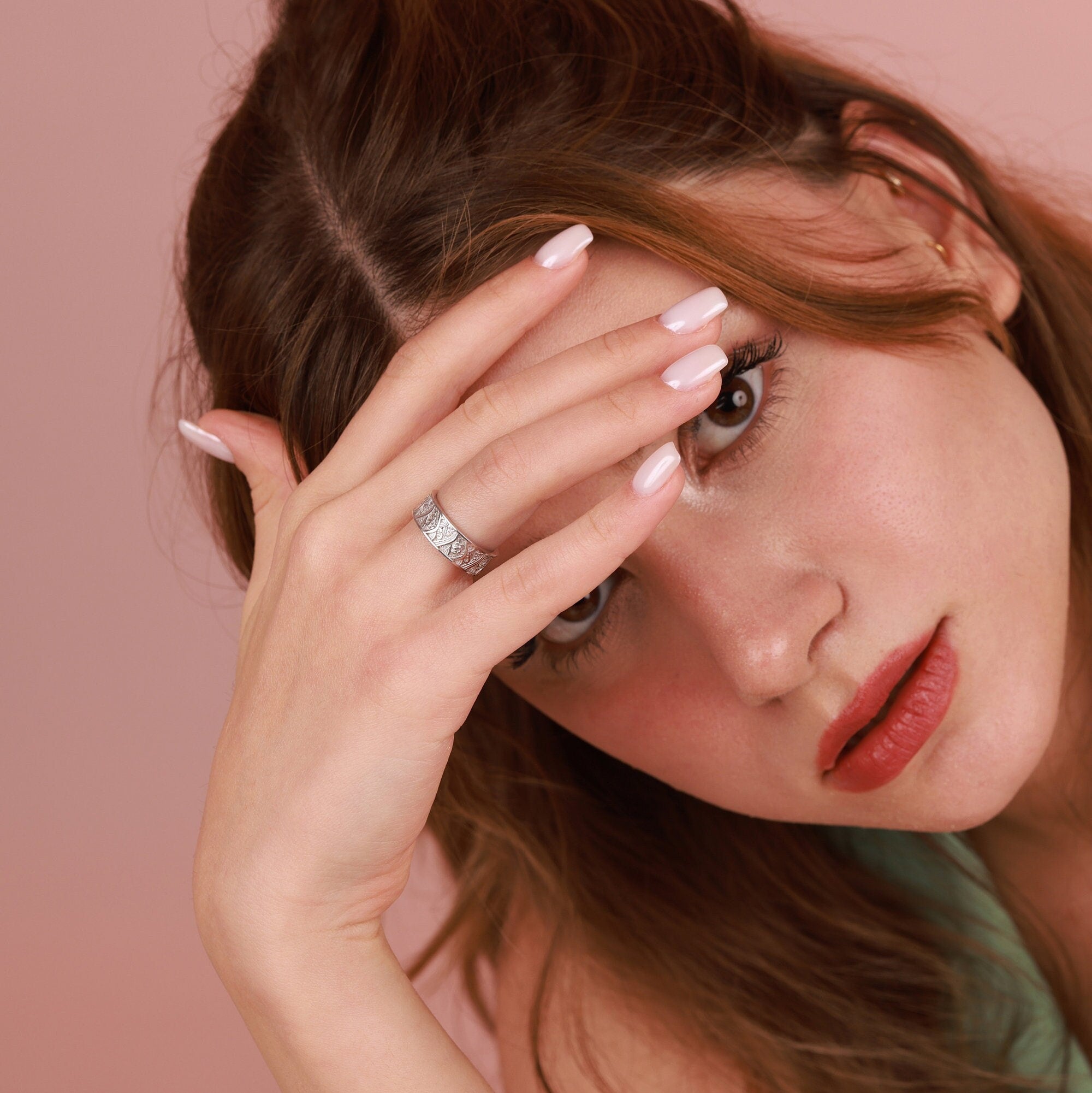 Woman with a polished silver ring on her finger against a pink background
