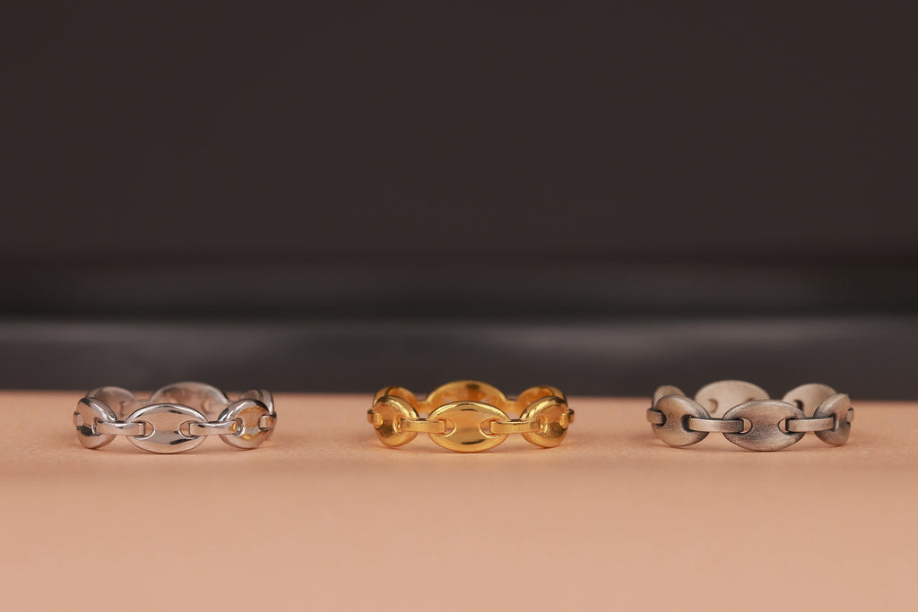 Three chain rings in silver, gold, and another silver design on a beige surface with a dark background.