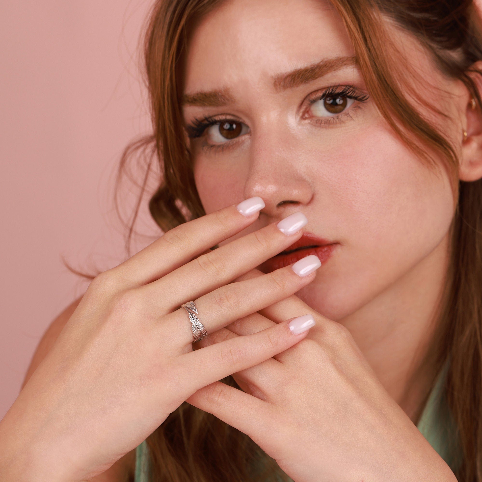 Woman wearing a polished silver feather wrap ring with a pink background
