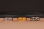 Three rings, two silver and one gold, on a brown surface with a dark background