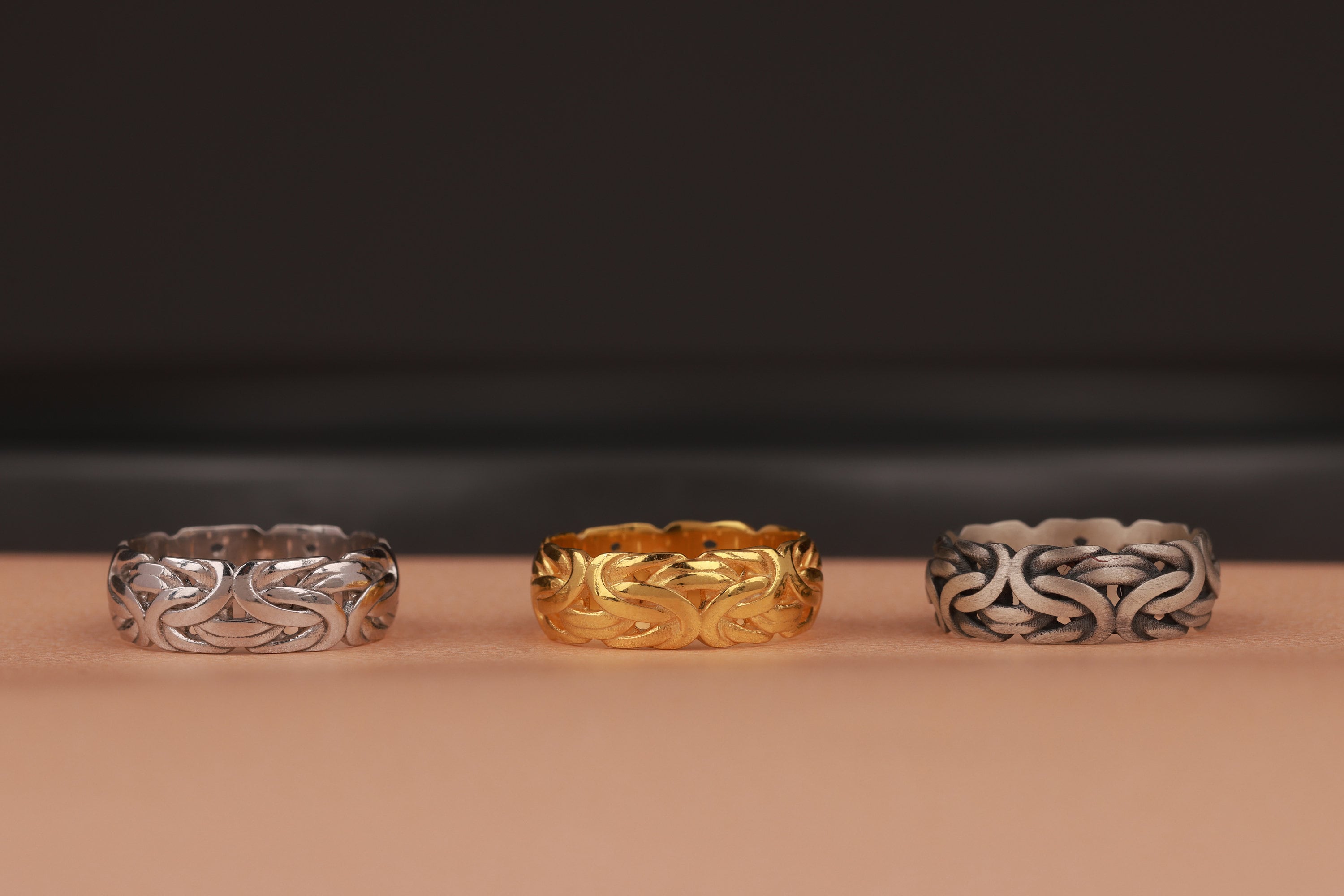 Three rings, two silver and one gold, on a brown surface with a dark background