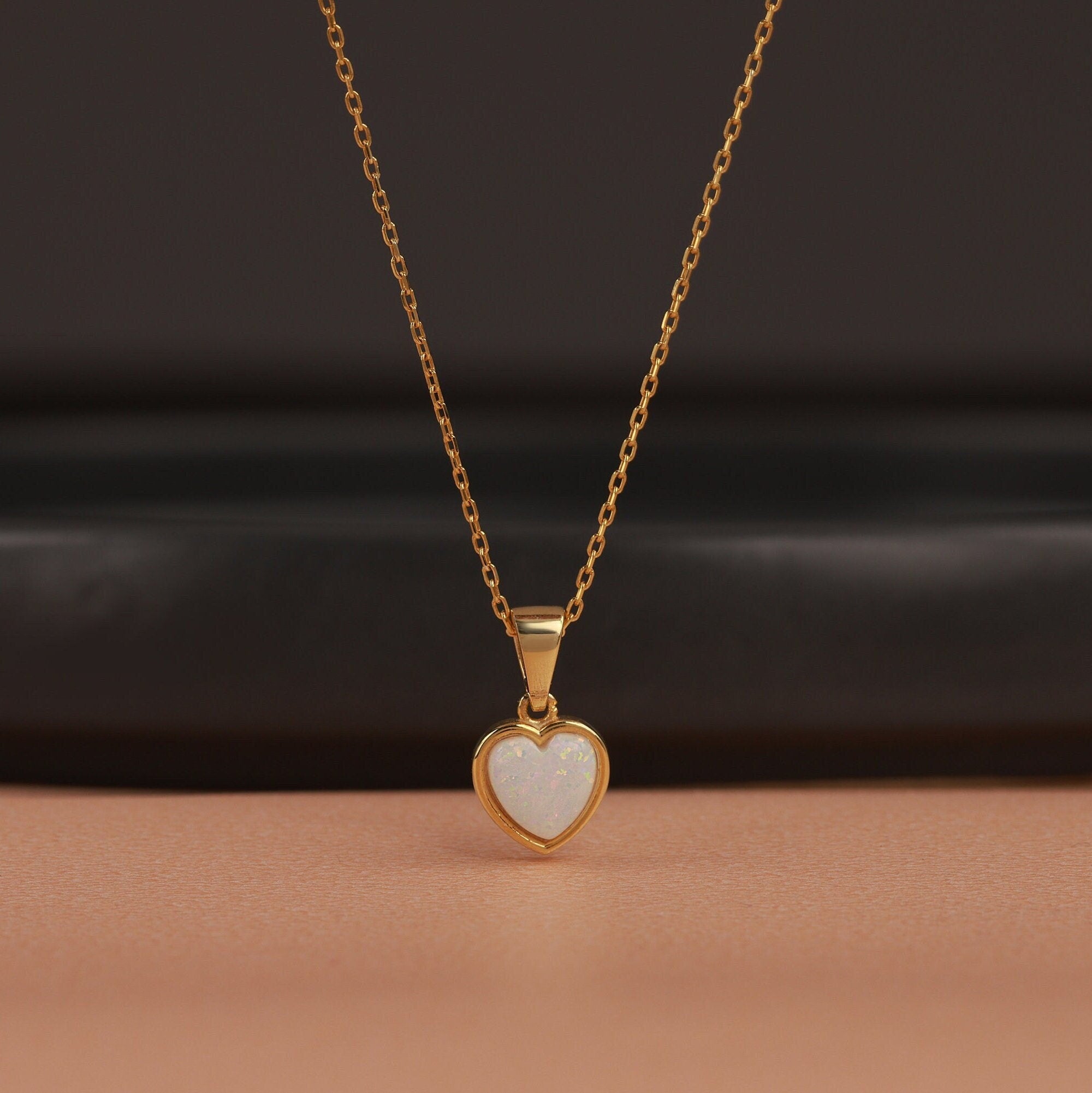 Gold necklace with a heart-shaped opal pendant on a dark background