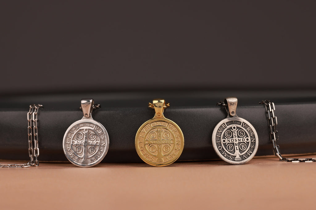 Three St Benedict cross pendants on a black and brown gradient background