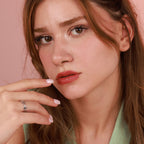 Close-up of a woman with a polished chain ring on her finger against a pink background