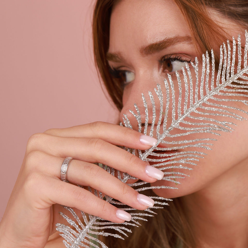 Woman holding a silver leaf against her face with a pink background