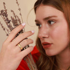 Woman holding dried lavender with a gold ring on her finger against a beige background