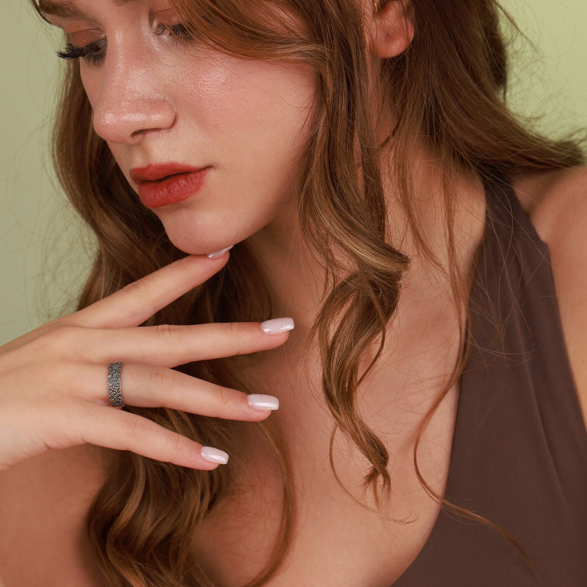 Close-up of a woman with red hair and a ring on her finger against a green background