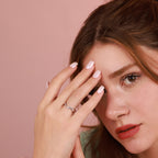 Close-up of a woman wearing a polished silver ring with a pink background
