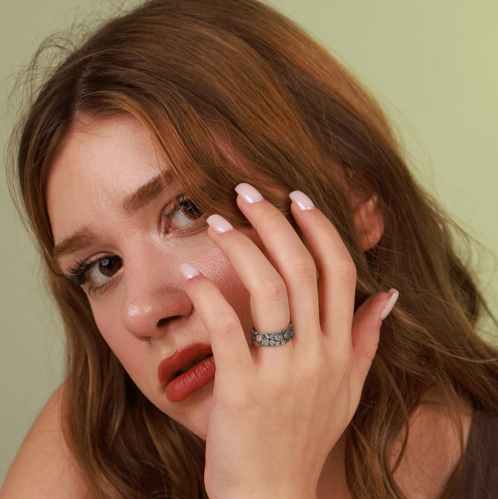 A woman applying makeup with a ring on her finger against a neutral background