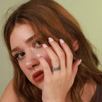 A woman applying makeup with a ring on her finger against a neutral background