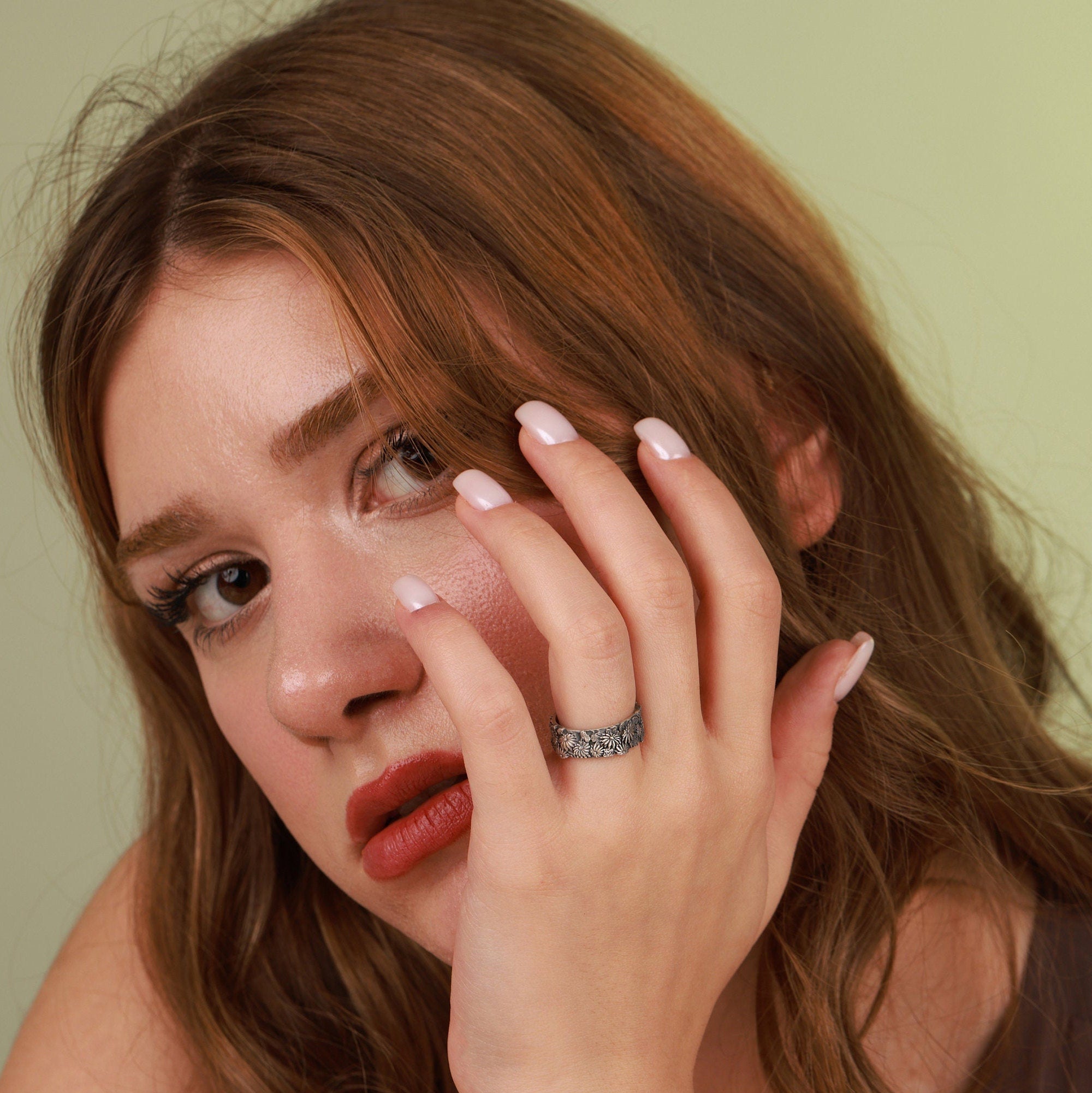 A woman applying makeup with a ring on her finger against a neutral background