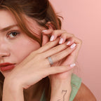 A woman wearing a diamond ring with a pink background