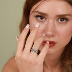 A woman with a silver ring on her finger touching her face against a neutral background