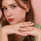 Close-up of a woman wearing a ring with a pink background