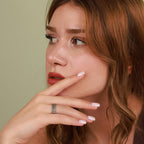 Woman with light makeup and a ring on her finger against a plain background