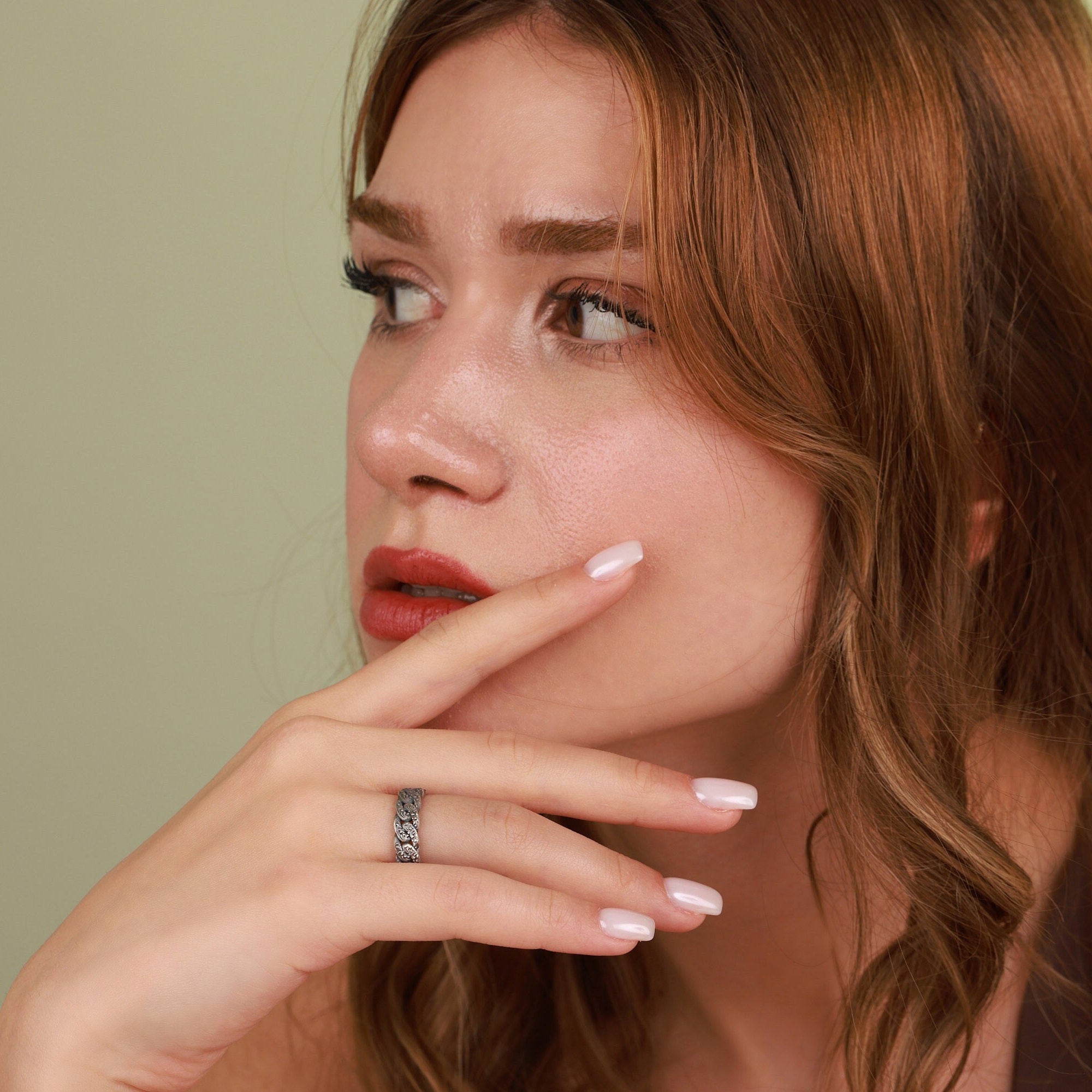 Woman with light makeup and a ring on her finger against a plain background