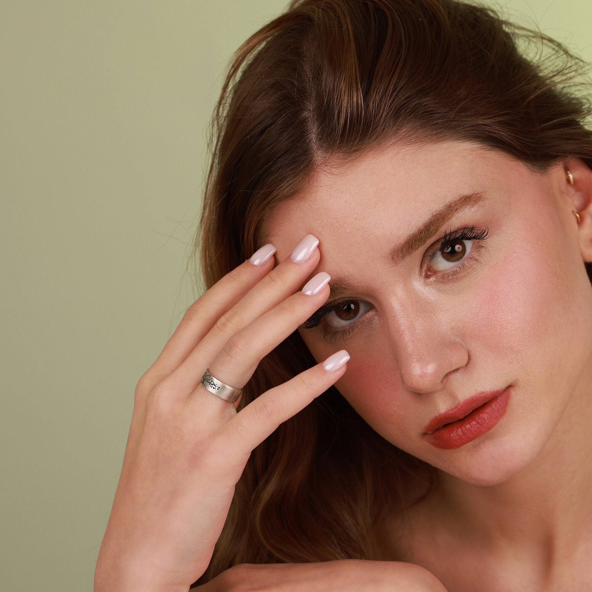 Woman with oxidized vintage wedding band ring on face against a green background