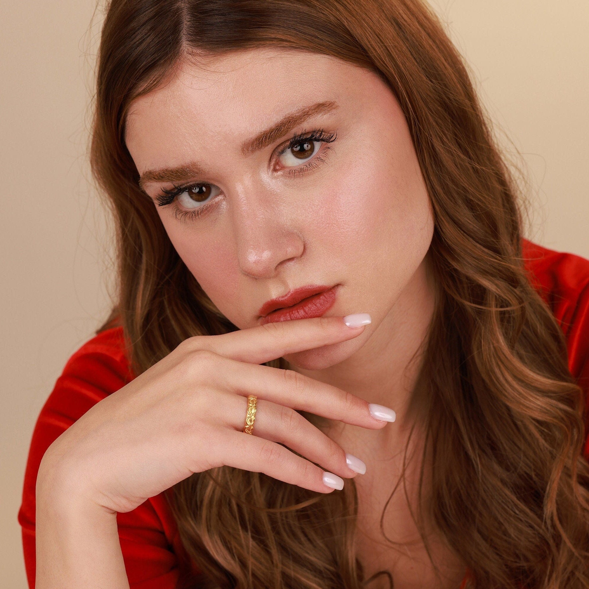 Woman with long brown hair wearing a red top against a beige background