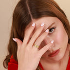 Woman with a gold vermeil wrap ring on her finger, holding her hand to her face against a beige background