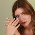 A woman with an angel wings ring on her finger against a green background