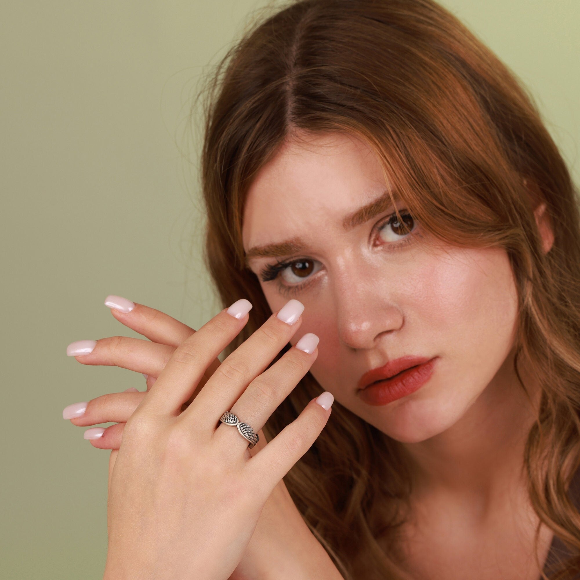 A woman with an angel wings ring on her finger against a green background