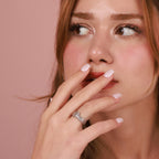 Woman with a  polished ring on her finger against a pink background