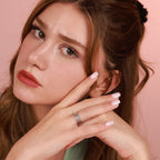 Woman with a ring on her finger against a pink background