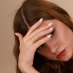 Woman with a gold ring on her finger against a beige background