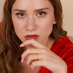 A woman wearing a gold band ring against a beige background