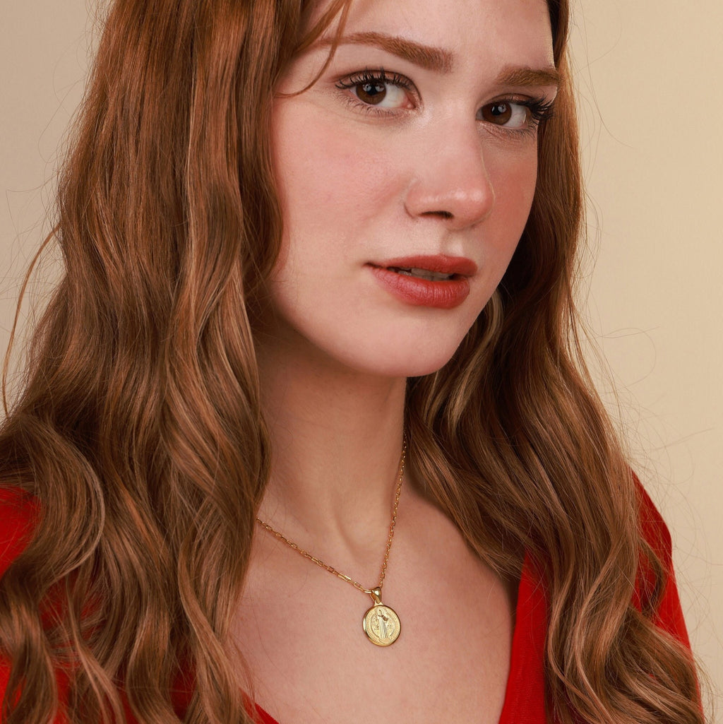 Woman wearing a gold coin necklace with a pendant against a beige background