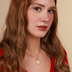 Woman wearing a gold coin necklace with a pendant against a beige background