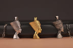 Three Egyptian-style Nefertiti bust pendants in gold, silver, and silver on a brown surface with a black background.