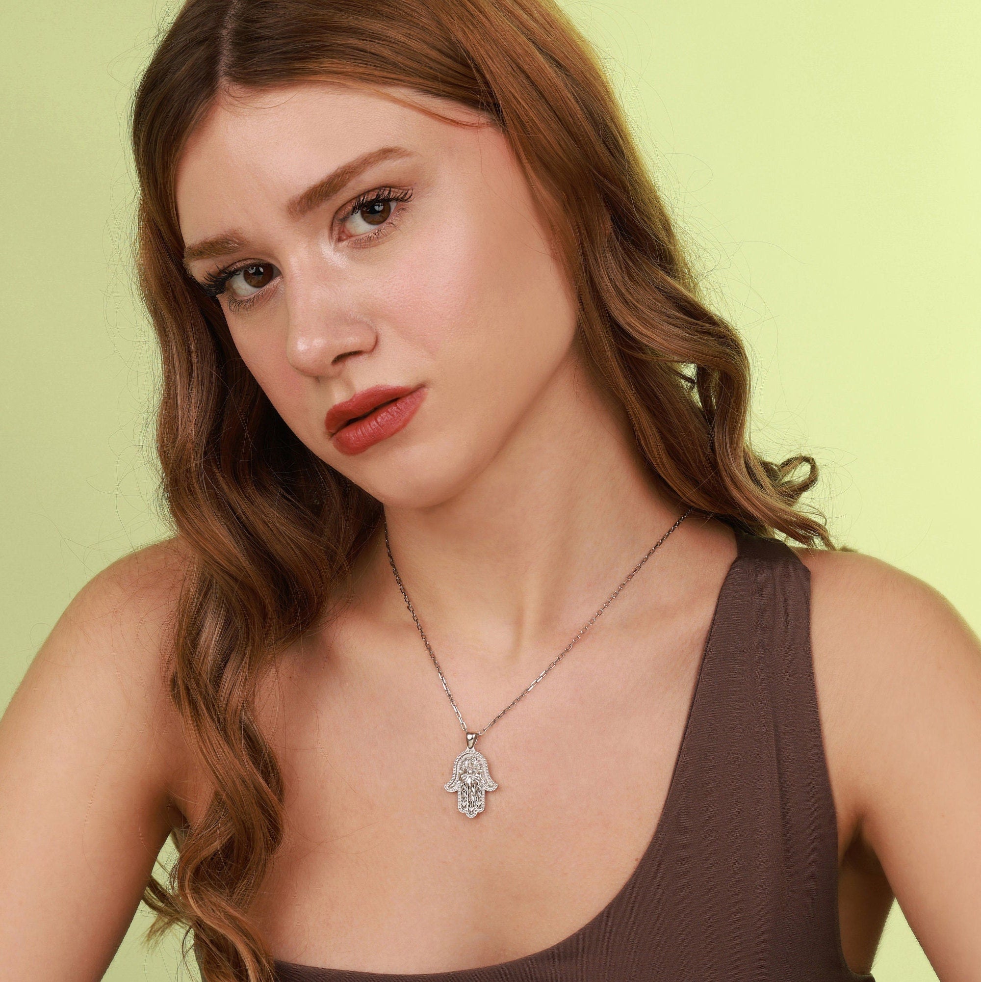 Woman wearing a polished sterling silver necklace with a hamsa hand pendant against a light green background