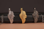 Three angel wing pendants in silver, gold, and bronze on a black and brown gradient background.