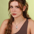 Woman wearing a polished silver ancel wing necklace with a green background